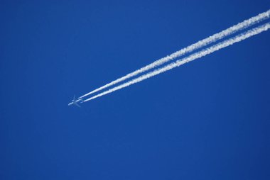 Mavi gökyüzünde uçan bir jet uçağı Parlak bir günde gökyüzünde uçağın izini sürüyor