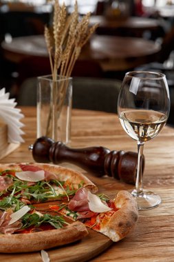 Jamonlu pizza ve ahşap bir masada otlar.