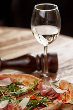 Jamonlu pizza ve ahşap bir masada otlar.