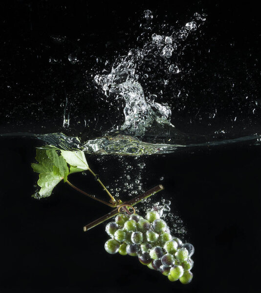 grape bunch falls into the water with splashes on a black background