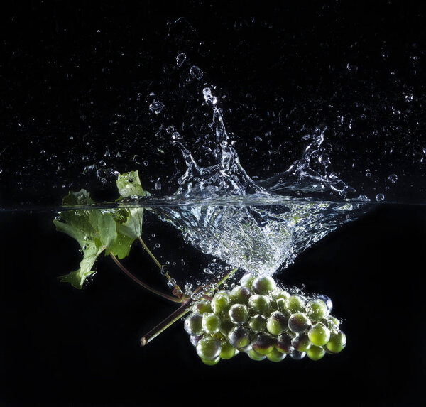 grape bunch falls into the water with splashes on a black background