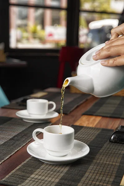 pour tea from a teapot into a cup on a wooden table, selective focus