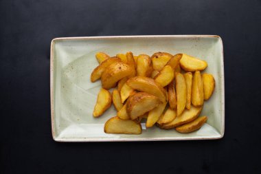 Koyu arkaplandaki tabakta kızarmış patates parçaları.