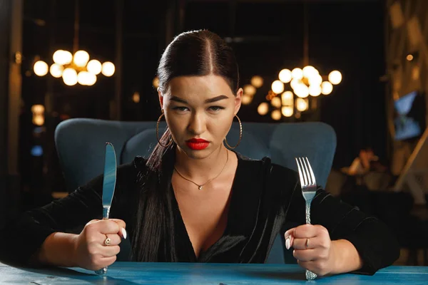 A hungry girl is waiting for food. Holding a knife and fork