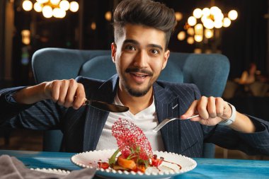 Genç bir adam masaya oturuyor ve yemek yiyor.