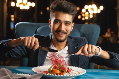 Genç bir adam masaya oturuyor ve yemek yiyor.