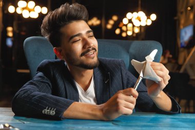 Aç bir adam yemek bekliyor. Çatal ve bıçak tutarken