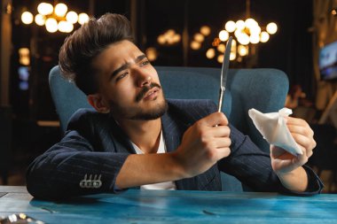 Aç bir adam yemek bekliyor. Çatal ve bıçak tutarken