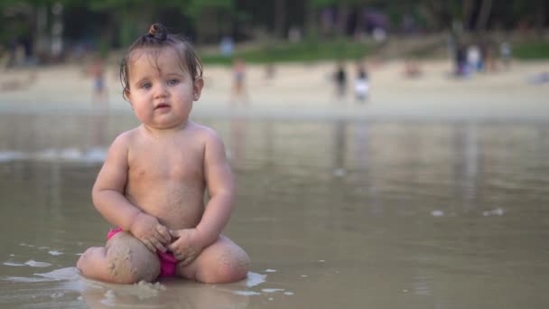 Cute little baby sitting on the beach and enjoying the waves — Stock Video