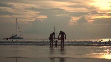 Mutlu bir aile deniz kıyısında yürüyüş. Siluetleri günbatımı.