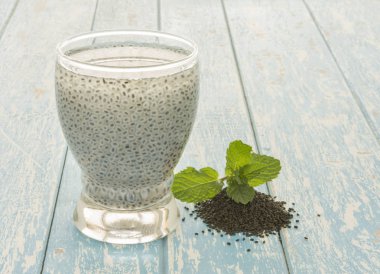 Woodden arka planda su bardakta tatlı fesleğen tohumu içeceği.