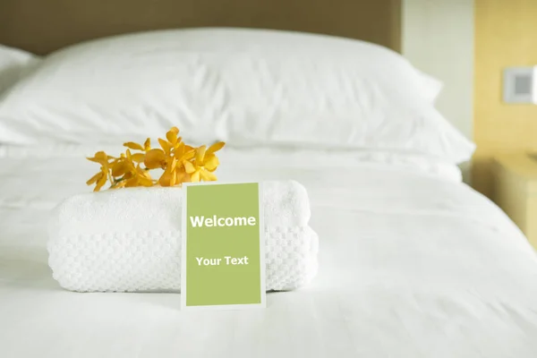 Welcome card placed inside a hotel room bed with White towel and Yellow orchid.