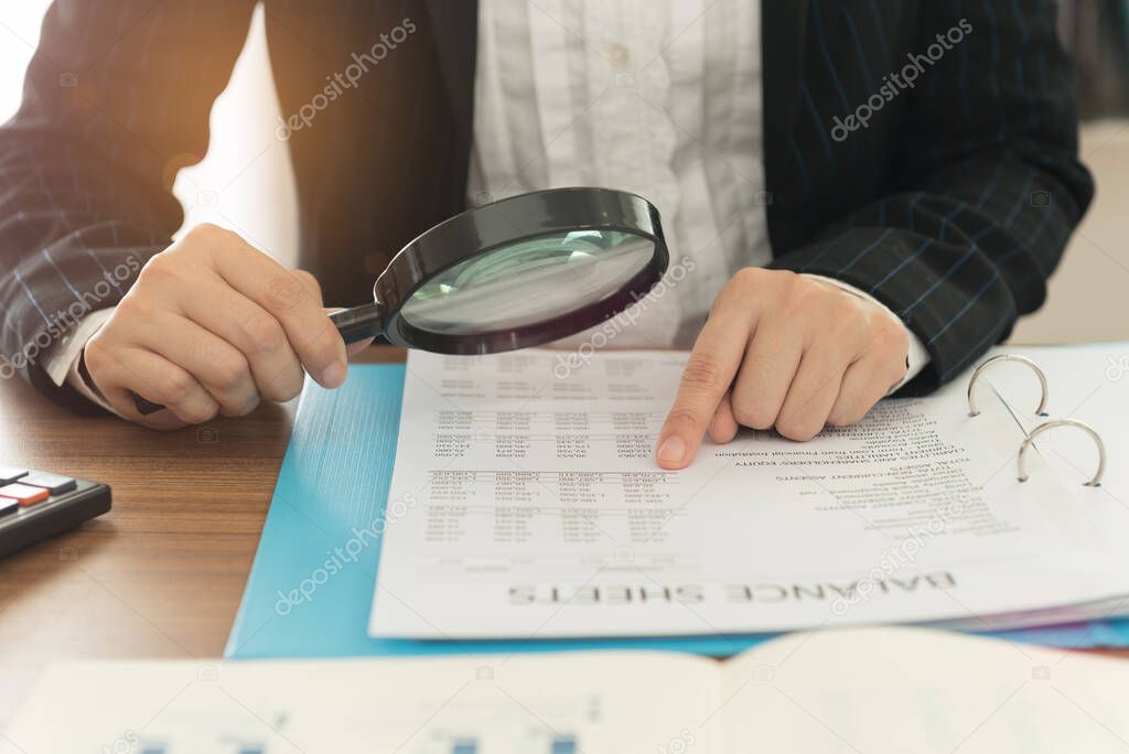Business women using magnifying to review balance sheet annual. Concept of Internal audit, Auditing tax,  Analyze return on investment.