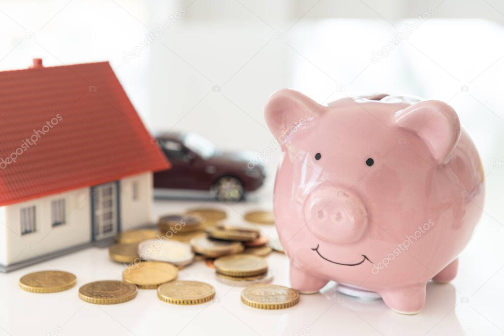 Pink piggy bank and a pile of money coins, cars, houses, and calculators. Financial concepts and saving.