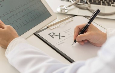 Dizüstü bilgisayarda kardiyogram çizelgesi ve reçeteli belge üzerine notlar arayan bir doktor..