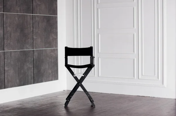 Svart hopfällbar stol framför en vit och grå vägg — Stockfoto