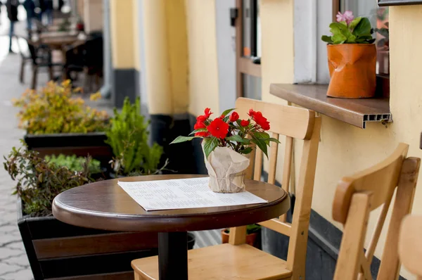 Dřevěný kulatý stůl s květinou na stole vedle café. — Stock fotografie