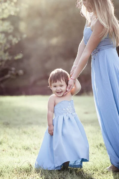 Yürümeye başlayan çocuk kız mavi uzun elbise anne ile gülüyor. — Stok fotoğraf
