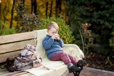 bir şık çocuk çocuk örme şal ve DRI ile bir bankta oturur