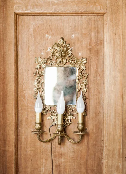 antique square mirror with lamps in the shape of candles in an ornamental gold frame on a wooden wall