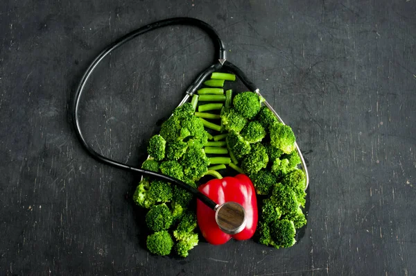 Diagnosis of heart condition. The broccoli, asparagus, pepper repeat the shape of the human heart and lungs, flat lay on dark background.