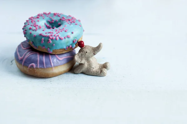 a small elephant figurine propped up with two different colored donuts, free space for text.