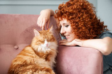 Kıvırcık saçlı, gülümseyen bir kız Kemerli kırmızı bir kediyi okşar