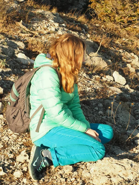 Dlouhé vlasy dívka sedící na kamenech, oblečený v nadýchané bundě — Stock fotografie