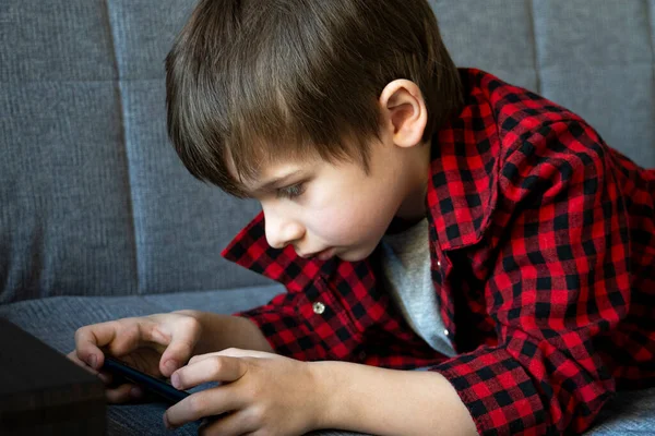 Enfocado chico con entusiasmo juega en un teléfono inteligente . — Foto de Stock