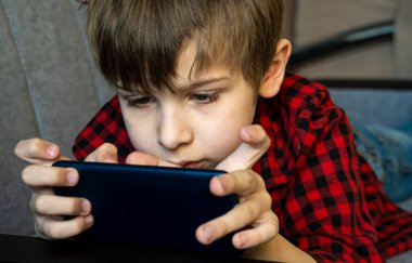 Odaklanmış çocuk hevesle akıllı telefonda oynuyor..