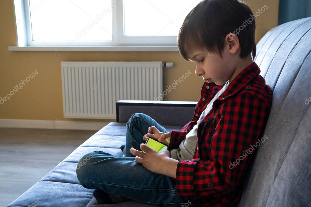 Focused boy enthusiastically plays in a smartphone.