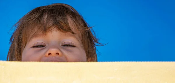 Primer plano de una niña traviesa y alegre mirando desde detrás de una tumbona . — Foto de Stock