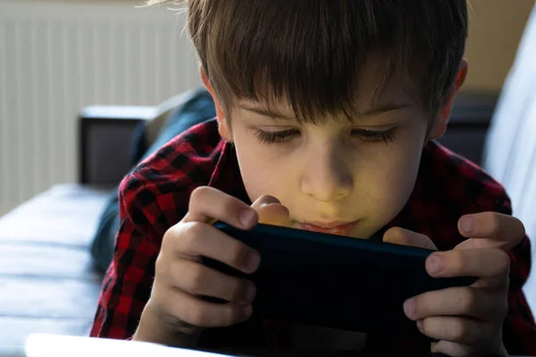 Enfocado chico con entusiasmo juega en un teléfono inteligente . — Foto de Stock