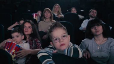 Gözlüklü çocuk sinemada film izlemek. Çocuk koltuğu geri karşı eğildi. Çocuk ve diğer insanlar sinema korkmuş korkunç an vardır.