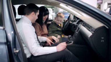 Gelecekteki sürücü araç içinde Bayilik test. Küçük çocuk yinelenen denetim tüm eylemleri anneler eller üzerinde otururken o satıcı gösterir. Araba satın alma bir araba Bayilik aile, potansiyel müşteriler. 