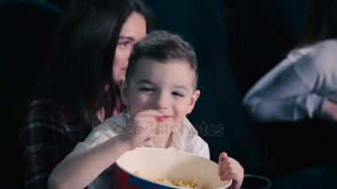Annemin elleri sinema oturan çocuk. Patlamış mısır yemek, gülen ve film izlerken çocuk.