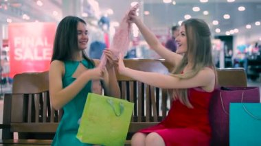 İki kız alışveriş merkezindeki bankta oturmuş. Alışveriş sonra trying belgili tanımlık atkı ve şapka kız.