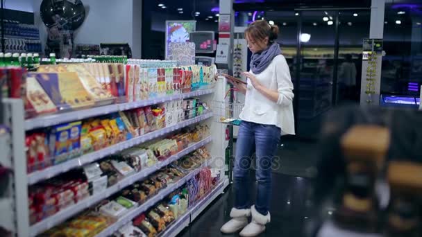 Dziewczyna wybiera produkty z tabletem. — Wideo stockowe
