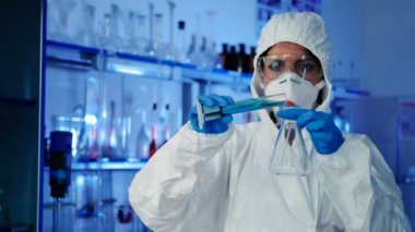 beyaz üniforma, maske ve mavi eldiven modern laboratuvar test tüpü ile çalışan genç kadın 