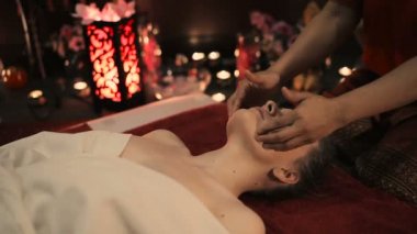 dişi kırmızı üniformalı spa salonda geleneksel Tay yüz masajı yapıyor 