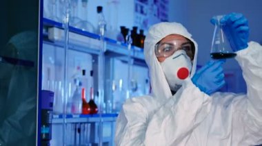 beyaz üniforma, maske ve mavi eldiven modern laboratuvar test tüpü ile çalışan genç kadın 