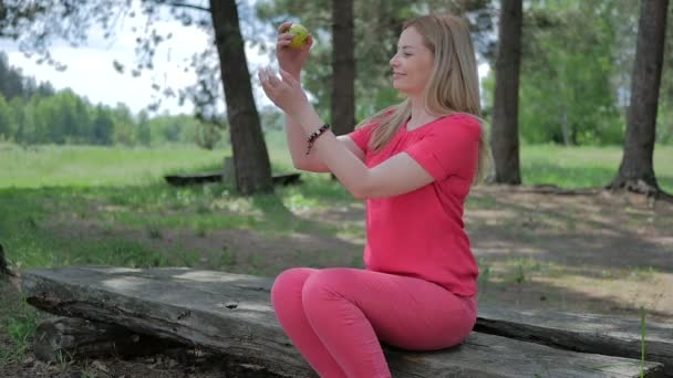 mladá blond žena v růžové oblečení jíst zelené jablko venku v přírodě  