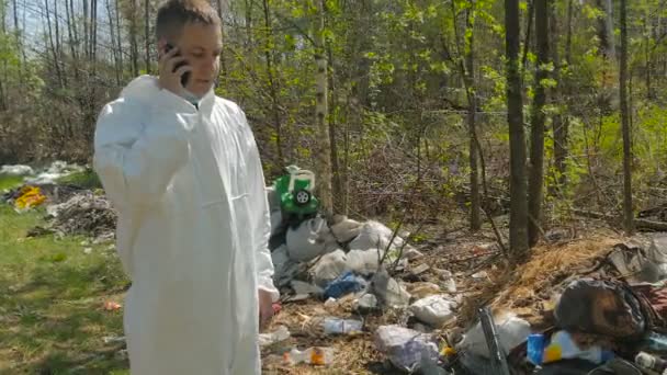 homme en uniforme blanc en utilisant le téléphone dans la forêt pleine d'ordures à la journée ensoleillée  