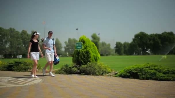 mladý muž a žena chůze na zelené trávě golfového klubu