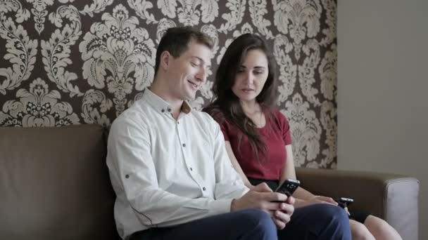 自宅のソファの上の携帯電話を使用して赤シャツの男とブルネットの女性実業家 — ストック動画