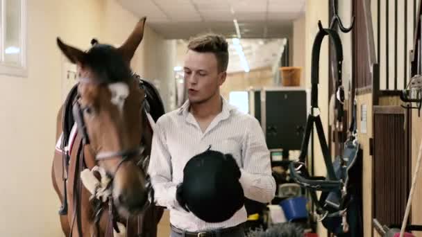 Homem segurando capacete preto no estábulo — Vídeo de Stock