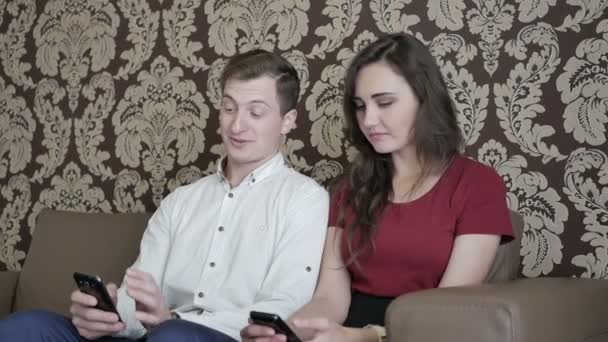 自宅のソファの上の携帯電話を使用して赤シャツの男とブルネットの女性実業家 — ストック動画