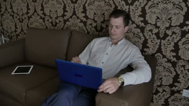 シャツはソファの上に座って 部屋でノート パソコンを使用してのビジネスマン — ストック動画