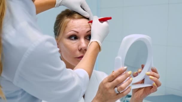 lékař pomocí červené pero do obličeje blond středního věku žena v kosmetologii kliniky