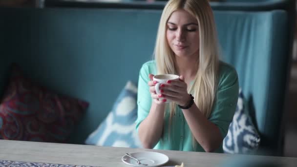 穿着绿色衬衣的年轻金发女郎在咖啡馆喝咖啡 — 图库视频影像